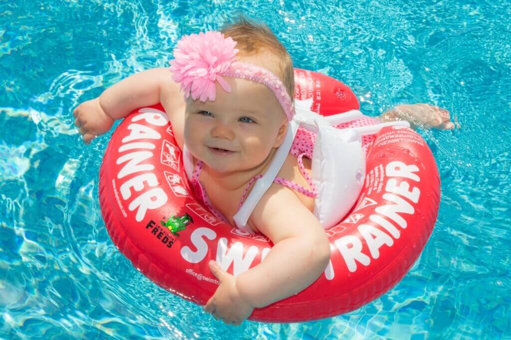 bouee-swimtrainer-bebe Un bébé souriant qui nage avec une bouée Swimtrainer rouge.