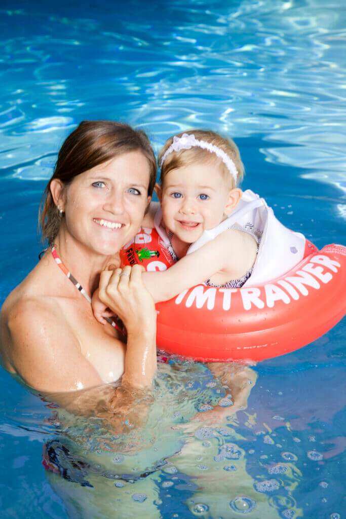 maman-enfant-nage Une mère et son enfant qui nage avec une bouée Swimtrainer rouge dans une piscine.